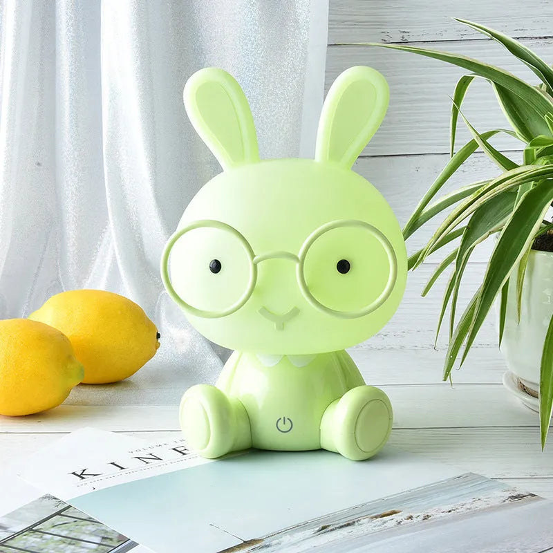 Blue plastic USB cartoon night light with a cute rabbit decoration wearing glasses on a desk.