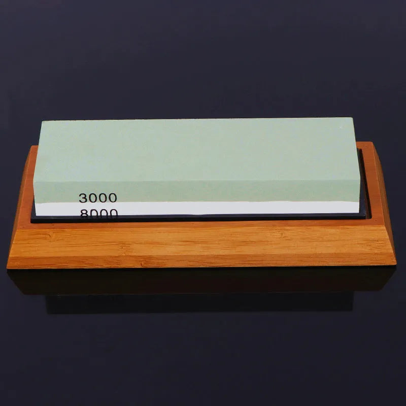 Red and white dual-grit kitchen whetstone on a bamboo base with sharpening accessories.