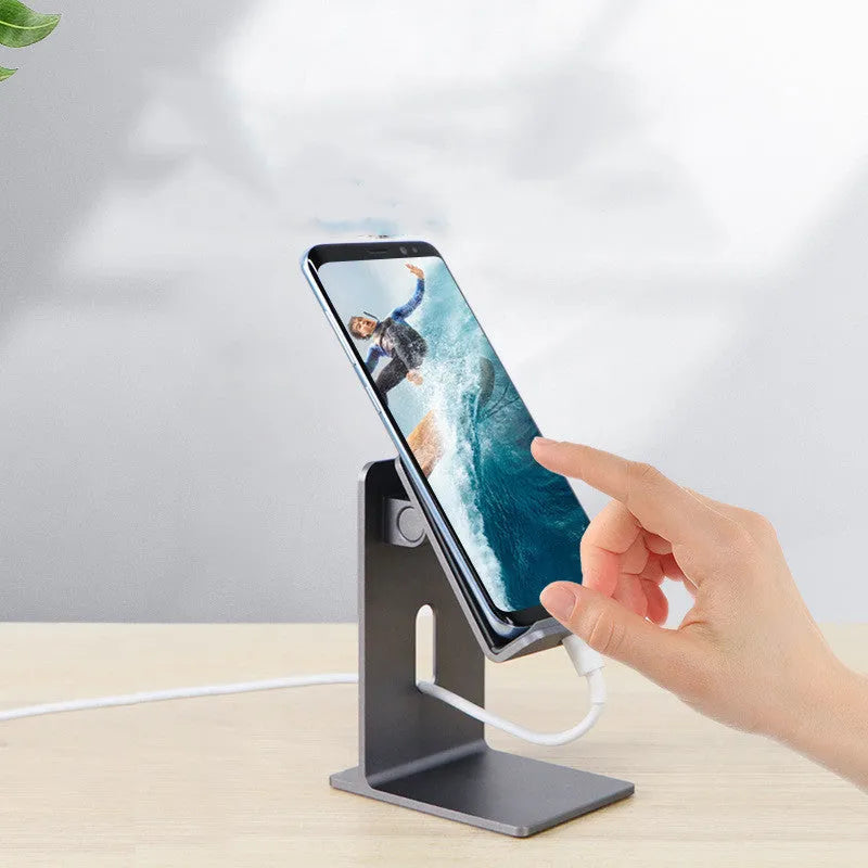 Dark space grey aluminium alloy mobile phone holder with adjustable clamp on a desk edge, holding a large tablet.