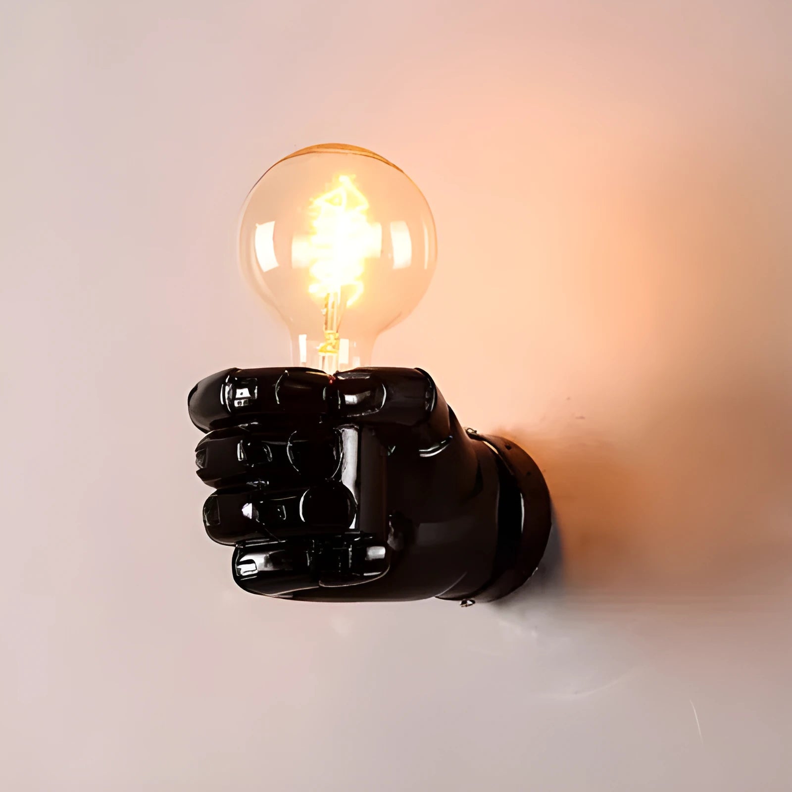 Close-up of a black resin fist sculpture wall lamp mounted on a dark wall, casting ambient light downwards.