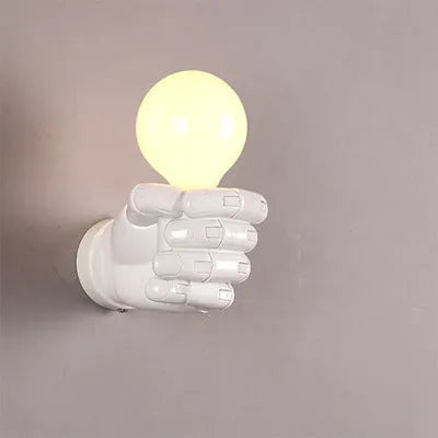 Close-up of a black resin fist sculpture wall lamp mounted on a dark wall, casting ambient light downwards.