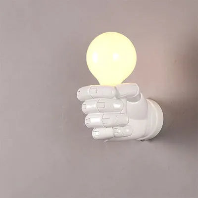 Close-up of a black resin fist sculpture wall lamp mounted on a dark wall, casting ambient light downwards.