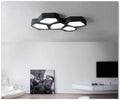 Modern geometric-shaped LED light with black iron frame and remote control on a side table.