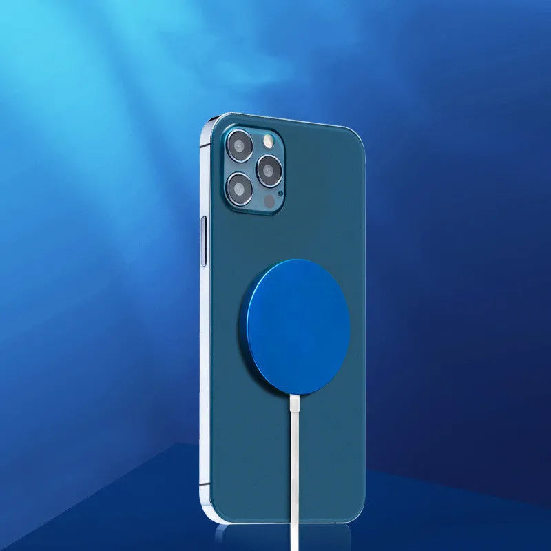 Silver metal Magsafe-compatible magnetic wireless charger for iPhone, shown next to a mobile phone.