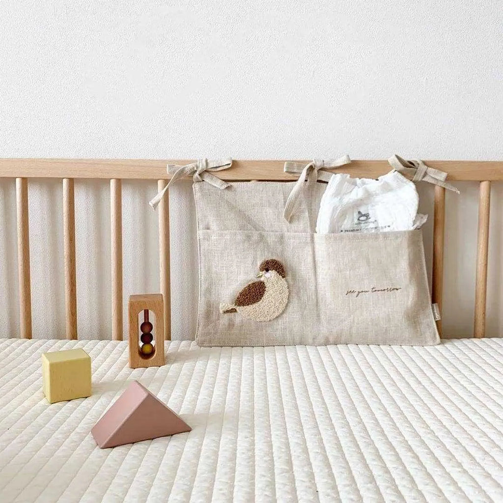 Khaki coloured cotton linen hanging storage bag with one large pocket beside a bed.