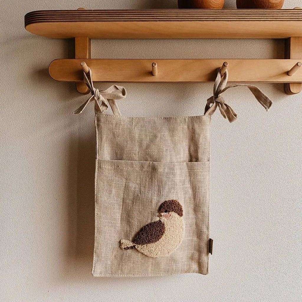 Khaki coloured cotton linen hanging storage bag with one large pocket beside a bed.