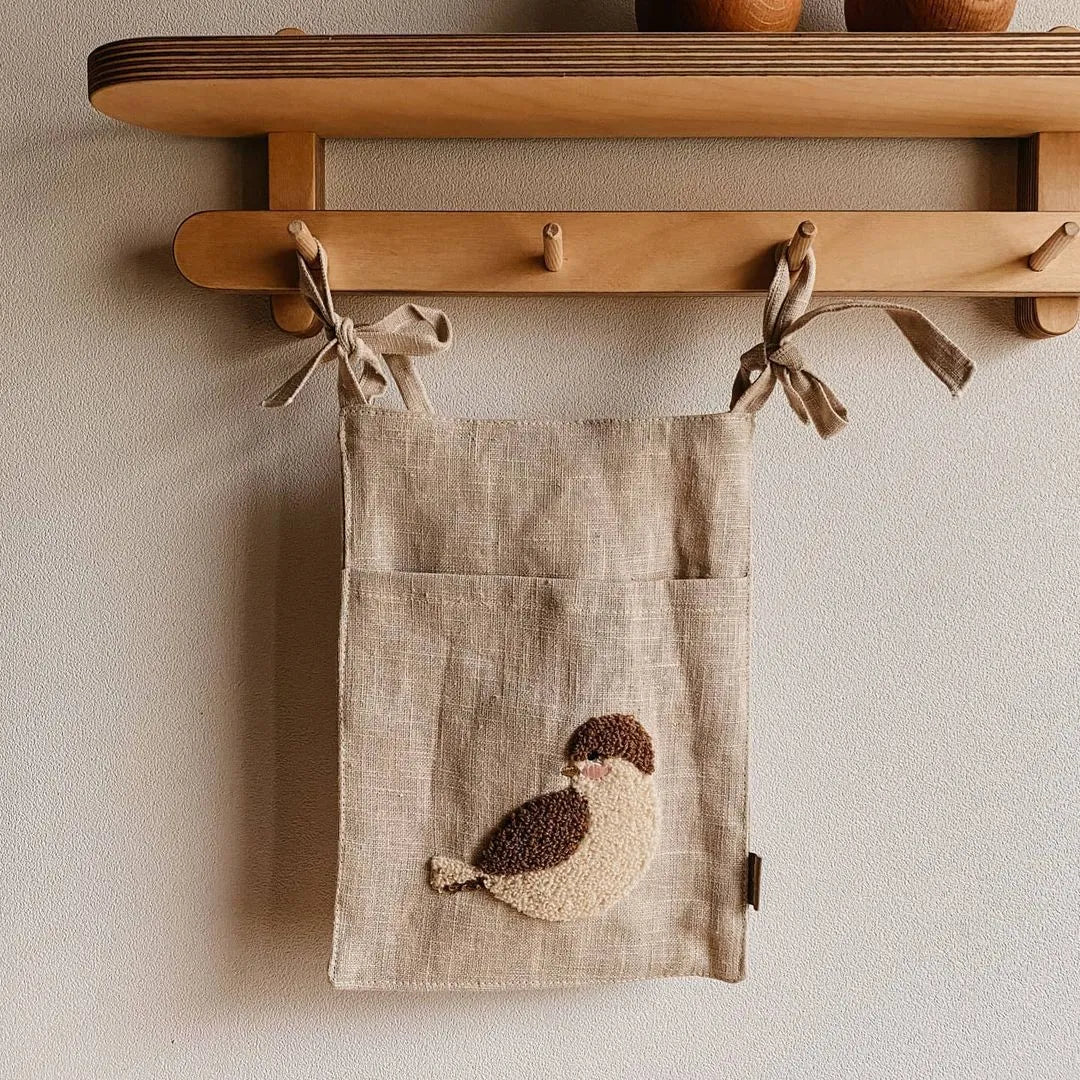 Khaki coloured cotton linen hanging storage bag with one large pocket beside a bed.