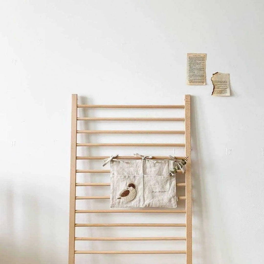 Khaki coloured cotton linen hanging storage bag with one large pocket beside a bed.