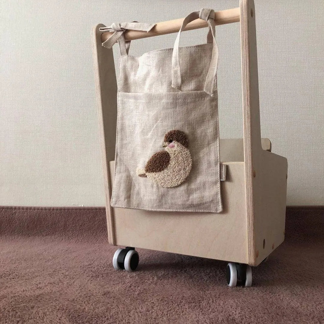 Khaki coloured cotton linen hanging storage bag with one large pocket beside a bed.
