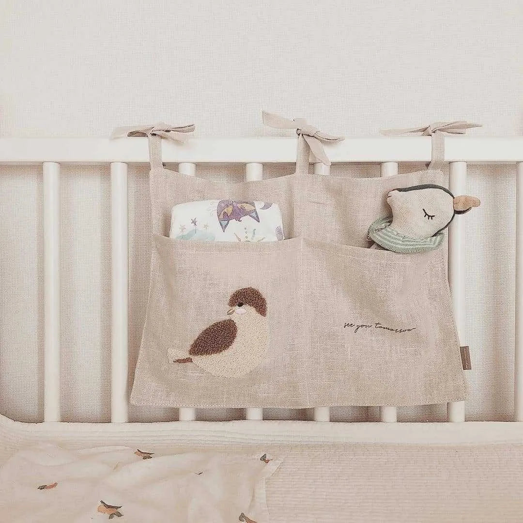 Khaki coloured cotton linen hanging storage bag with one large pocket beside a bed.