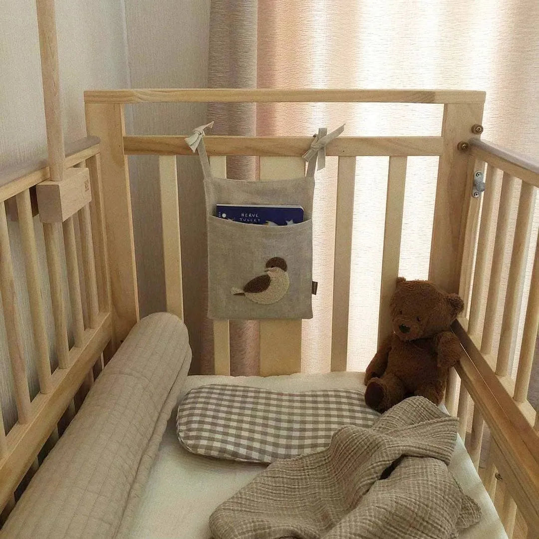 Khaki coloured cotton linen hanging storage bag with one large pocket beside a bed.