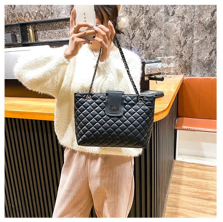 Large women's PU leather tote bag with lock closure and chain shoulder strap in horizontal square shape on white background