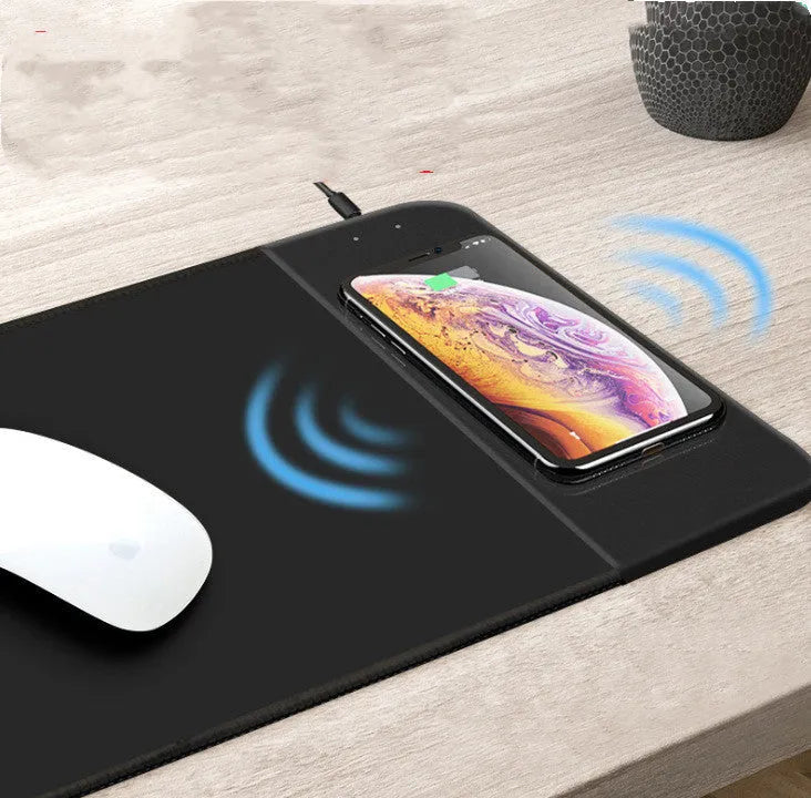 Black cartoon wireless charging mouse pad with glowing RGB lights on a desk.