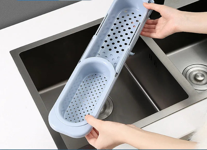 Blue grey telescopic sink rack holding a sponge and soap bar next to a kitchen tap