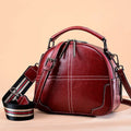 Wine red round leather handbag with soft double handles and a zipper top, shown front-on.