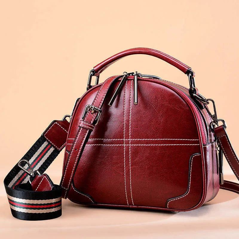 Wine red round leather handbag with soft double handles and a zipper top, shown front-on.