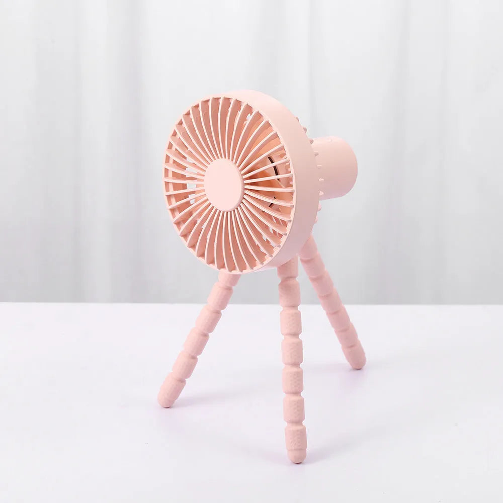 Small black adjustable tripod desktop fan with bending neck and clip, shown on a desk.