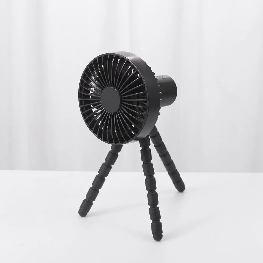 Small black adjustable tripod desktop fan with bending neck and clip, shown on a desk.