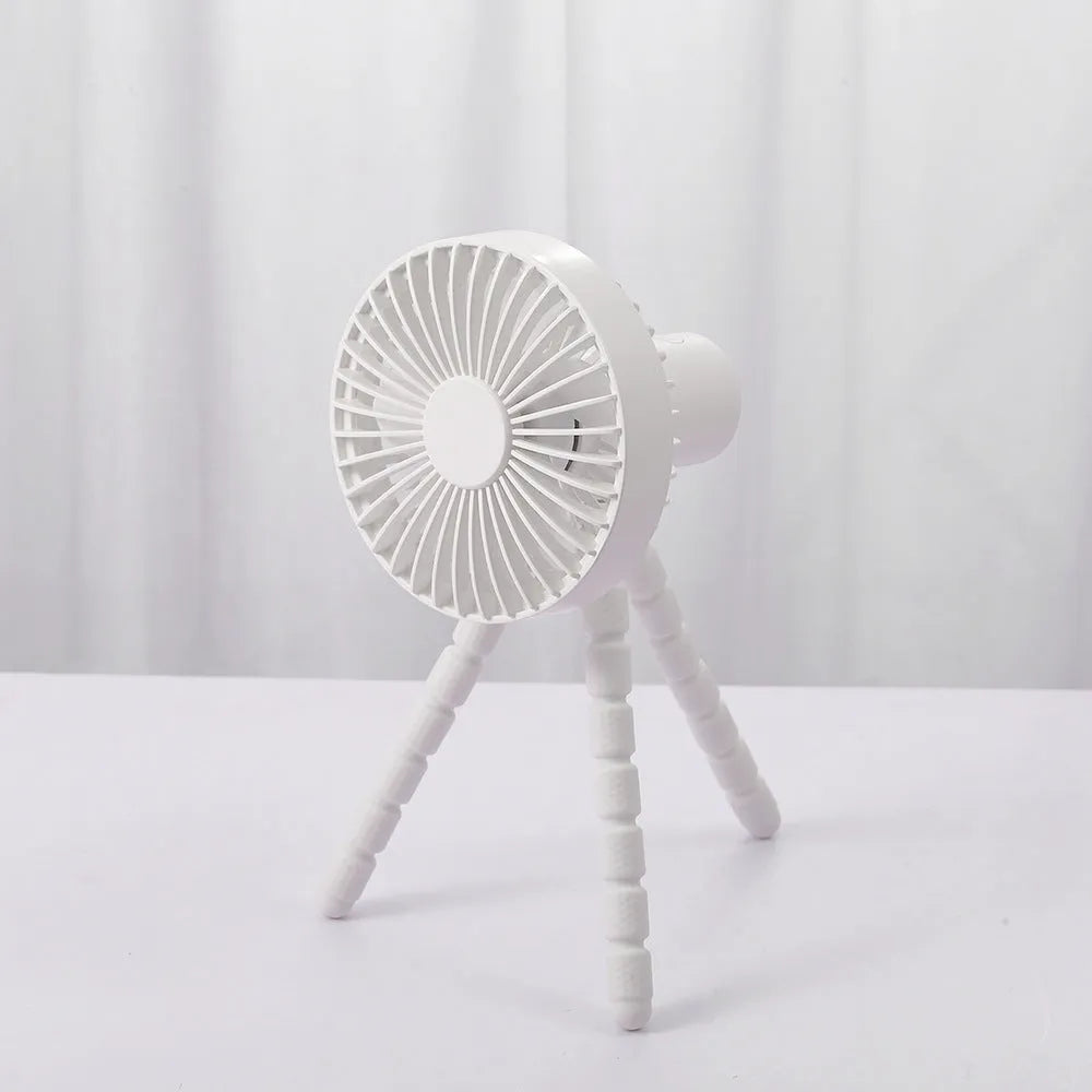 Small black adjustable tripod desktop fan with bending neck and clip, shown on a desk.