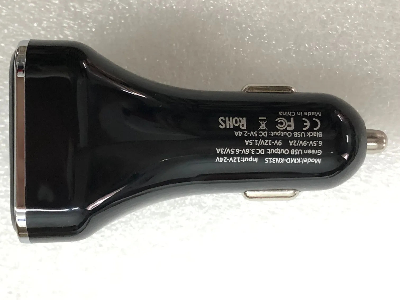 Black dual USB car charger with LCD screen displaying voltage, plugged into a car dashboard socket.