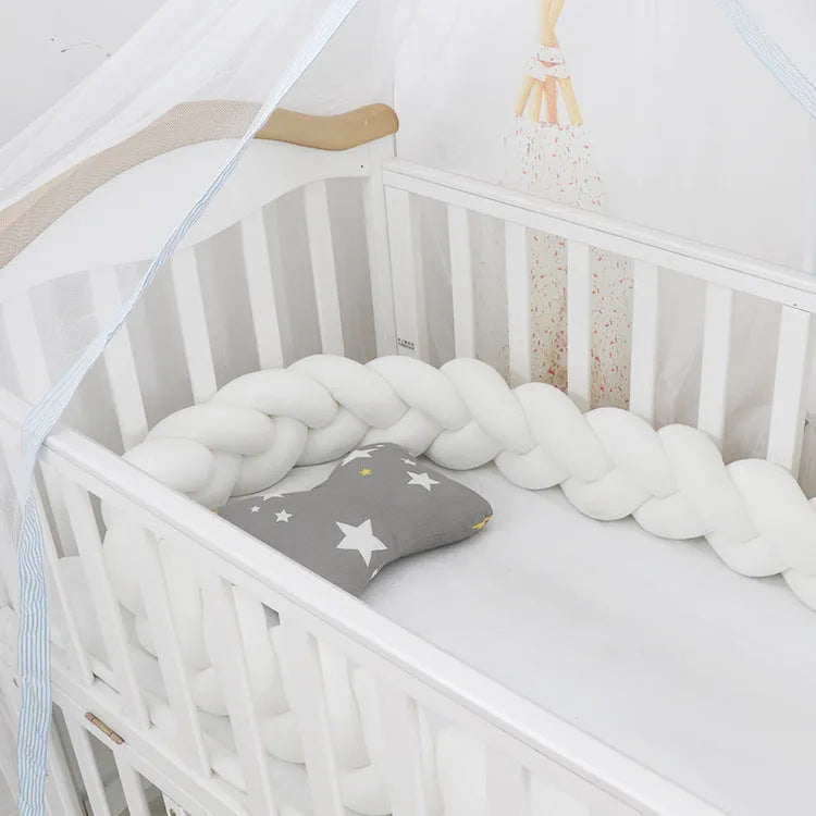 Braided knot style crib bumper in spandex velvet, wrapped around white cot rails in a nursery.