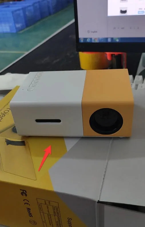 Mini LED projector YG300 in white and yellow, with lens and ventilation grilles, on a table