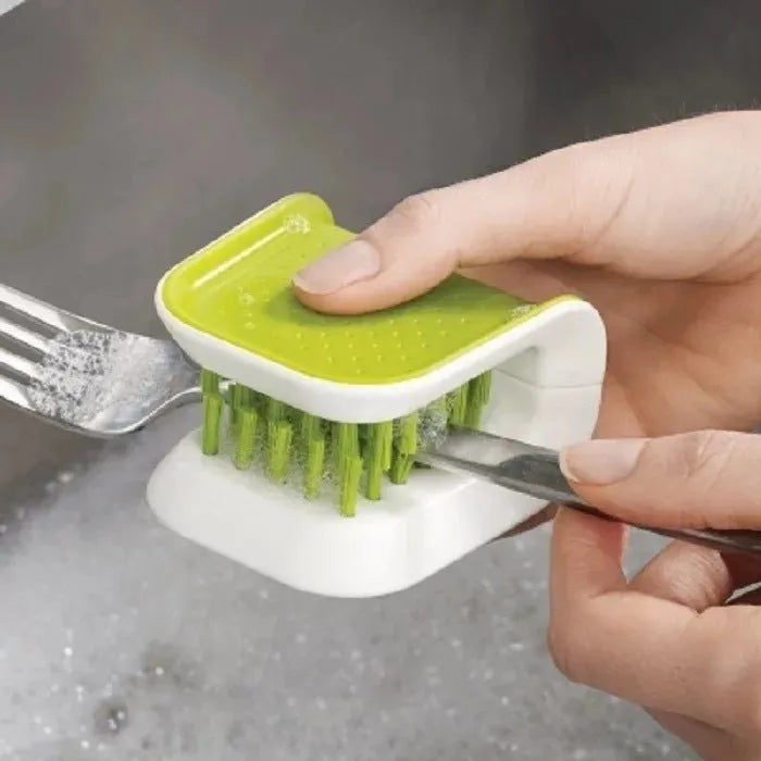 Blue U-shaped plastic brush for cleaning kitchen knives and forks on a draining board.