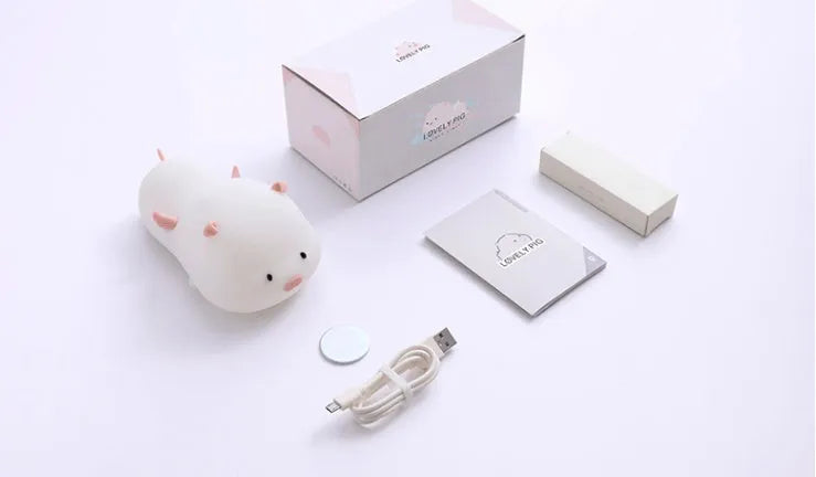 Pink silicone night light in the shape of a sleeping pig on a table.