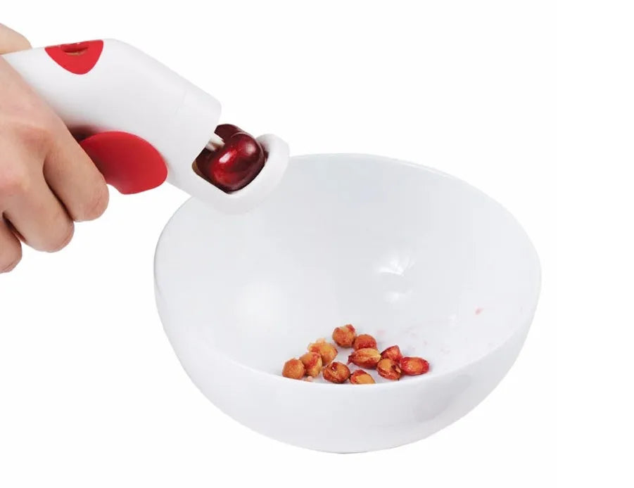 Stainless steel manual cherry pitter tool with protective end caps on a wooden surface.