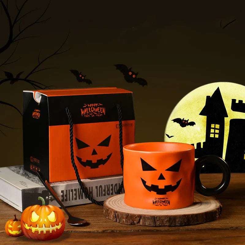 Orange ceramic pumpkin-shaped mug with handle on a table beside a dessert spoon and gift box.