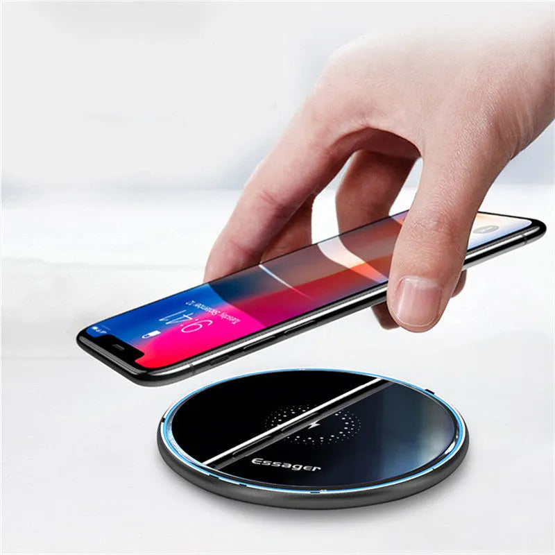 Black aluminium wireless charging pad on a desk with a mobile phone charging on top.