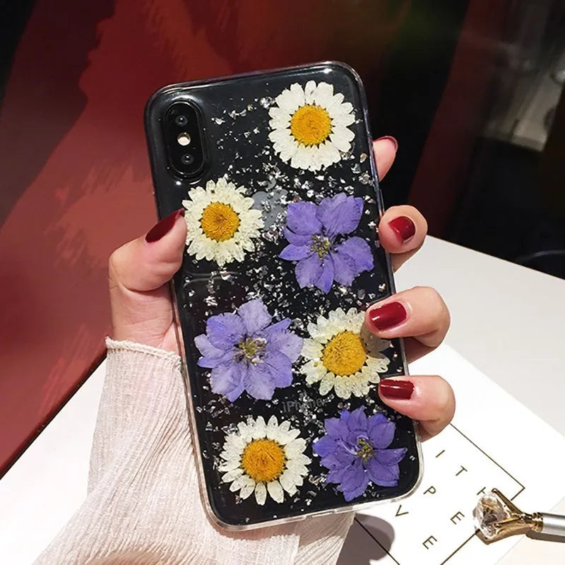 Clear TPU iPhone case showing real pink dried flowers encapsulated in epoxy resin on the back.