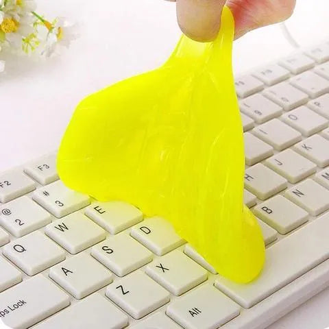 Blue magic cleaning gel putty being pressed onto a laptop keyboard to remove dust.