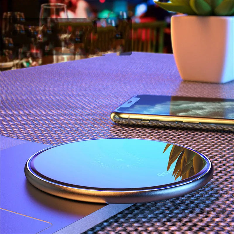 Black aluminium wireless charging pad on a desk with a mobile phone charging on top.