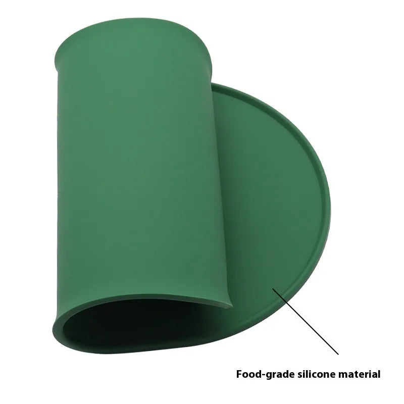 Beige silicone cat feeding mat with raised edge containing a food bowl and scattered kibble on a kitchen floor.