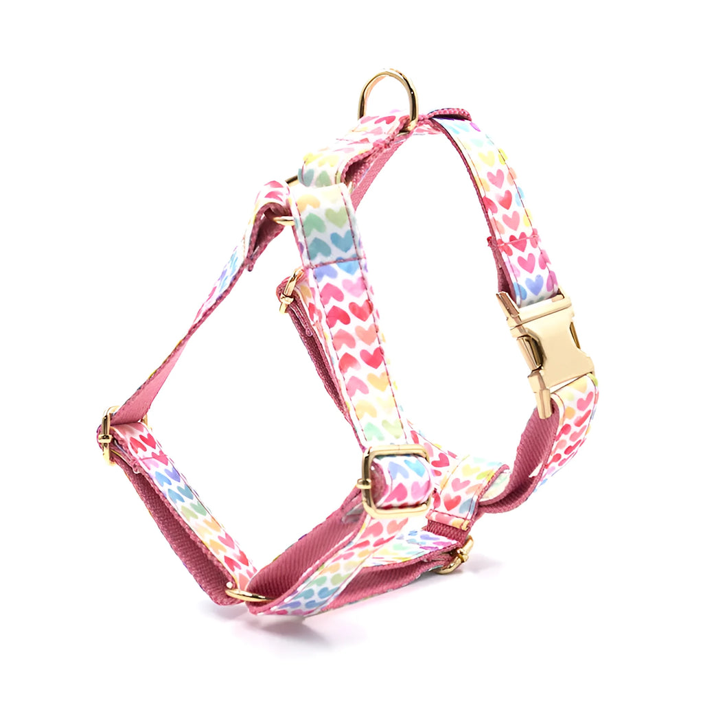 Pink dog harness with gold buckle and heart-shaped stone decoration on white background