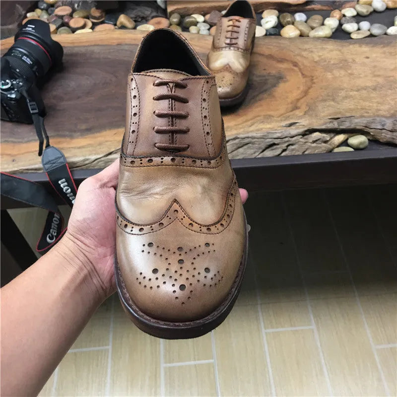 Men's light brown leather lace-up shoes with hand-carved distressed detailing on a wooden background.