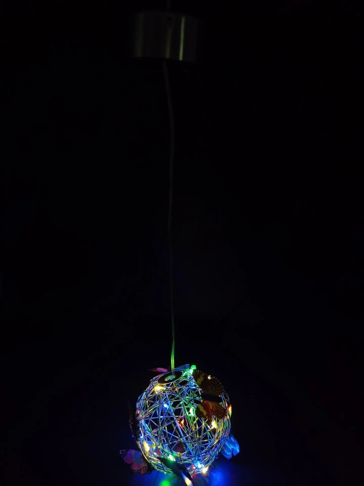 White outdoor solar ball light with random colour butterfly decorations on a garden lawn