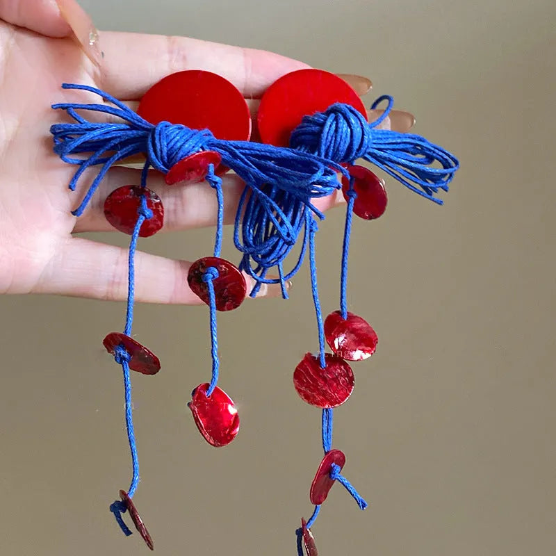 A pair of geometric cloth earrings with a blue resin flower decoration and silver needle detail.