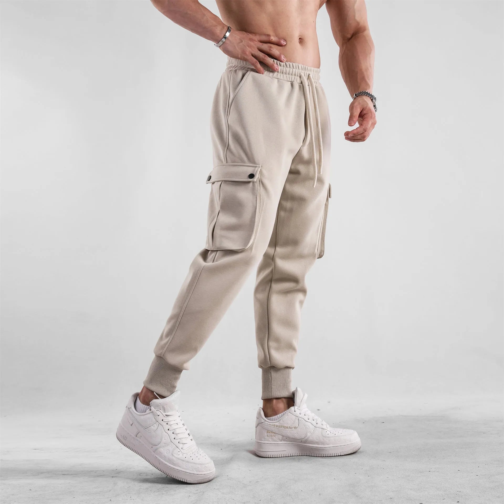 Men's loose-fit beige cotton trousers with tied ankle cuffs and multiple pockets on a neutral background.