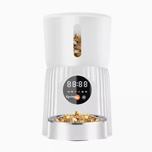 Black automatic pet feeder with digital display and food hopper on a wooden floor.