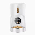 Black automatic pet feeder with digital display and food hopper on a wooden floor.