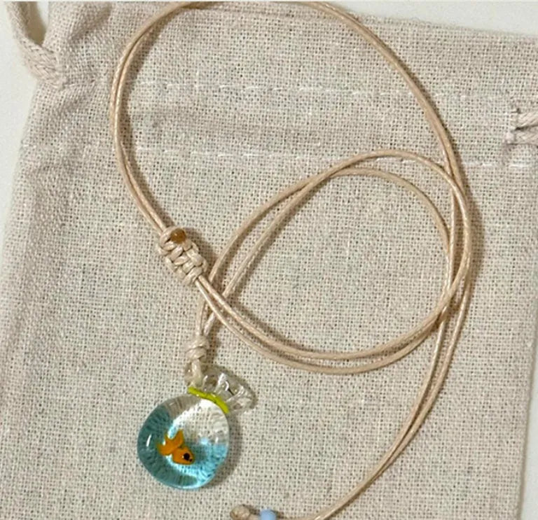 Women's necklace with a blue hand-painted fish charm on a beige cotton and linen clavicle chain.