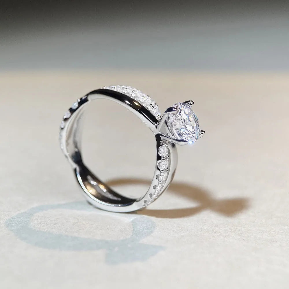 A silver ring with a 1 karat moissanite stone in a four-claw setting on a twisted geometric band.