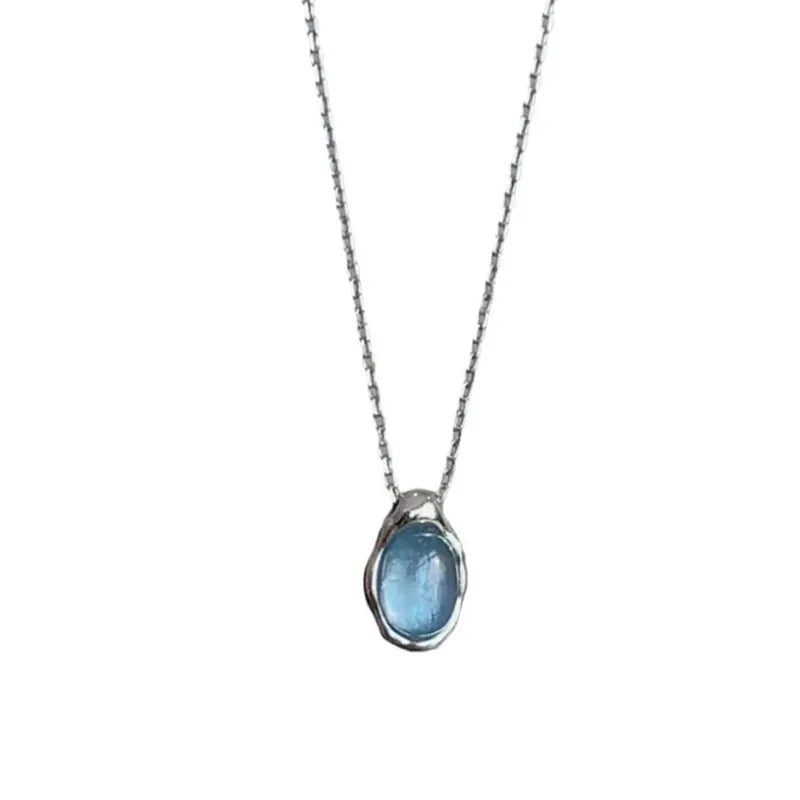 Close-up of a navy blue water drop pendant necklace with a platinum-colour finish on a textured cross chain.