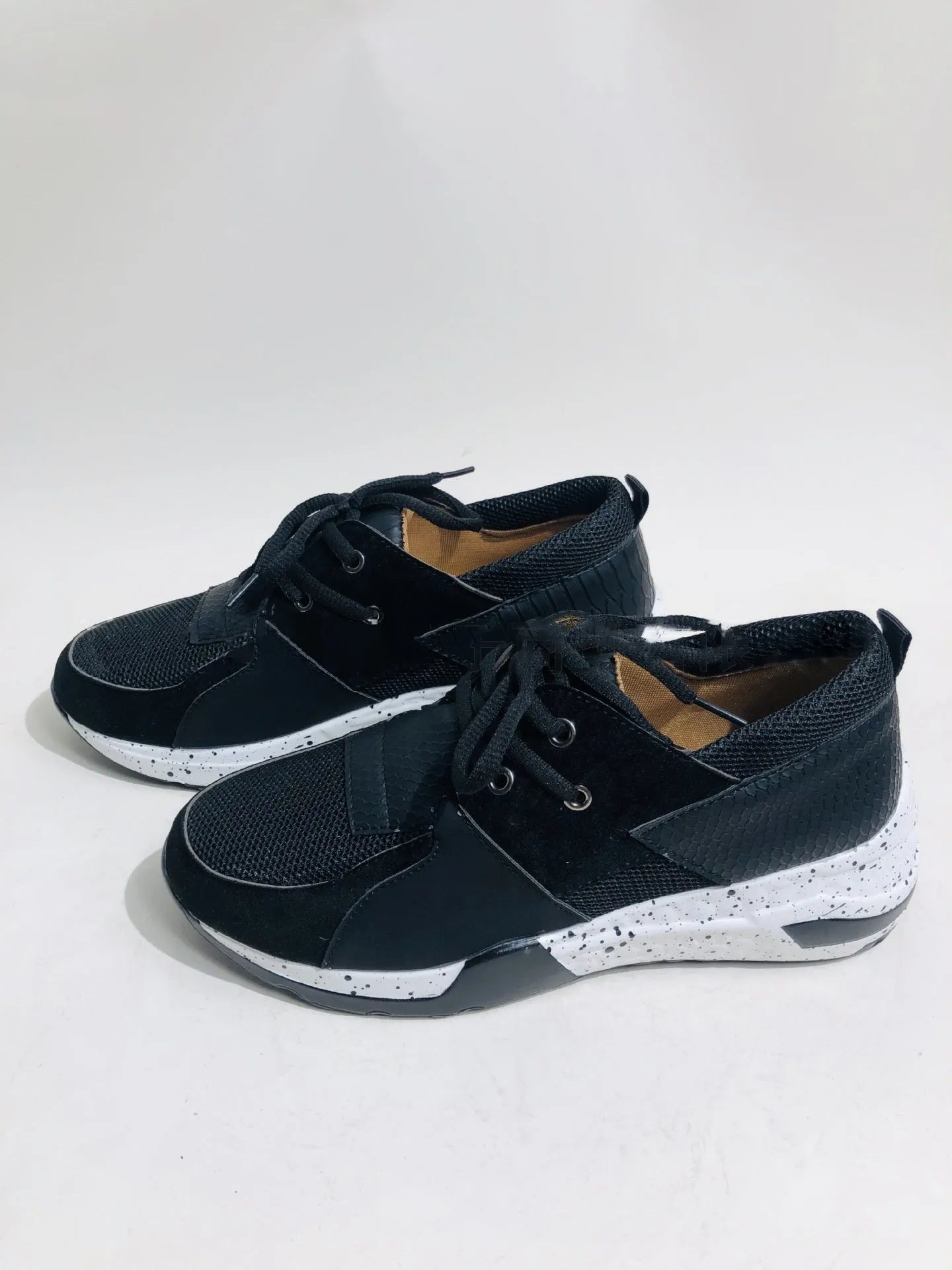 Women's black suede wedge sneakers with a low-cut ankle and round toe on a wooden floor.