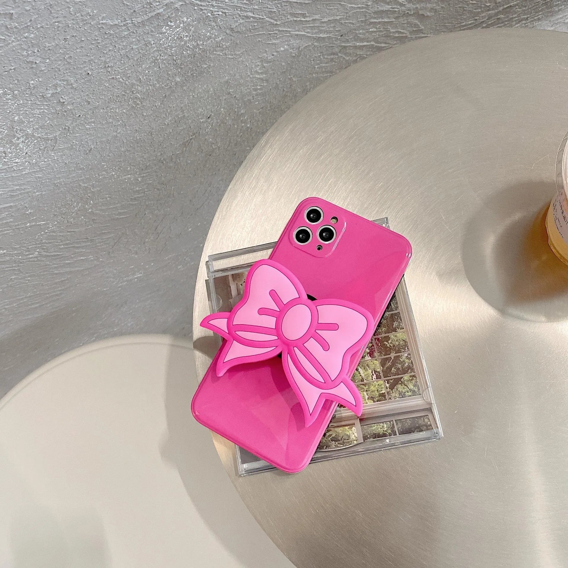 Rose red iPhone case with a pink bow design and a fold-out kickstand on the back.