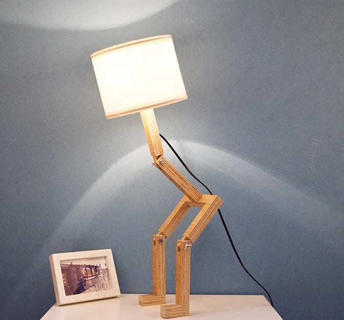 Creative humanoid wooden table lamp with white fabric shade and deformable design on a wooden surface