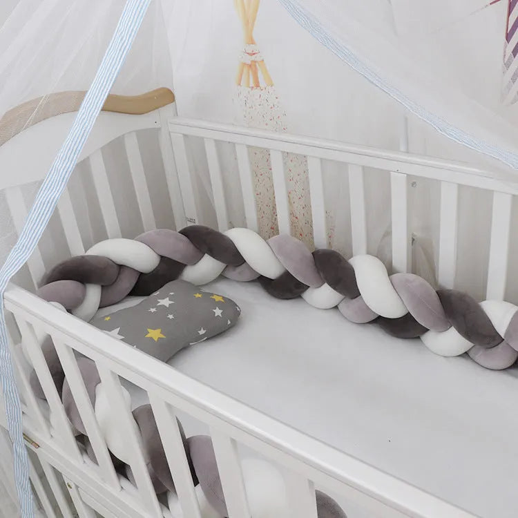 Braided knot style crib bumper in spandex velvet, wrapped around white cot rails in a nursery.
