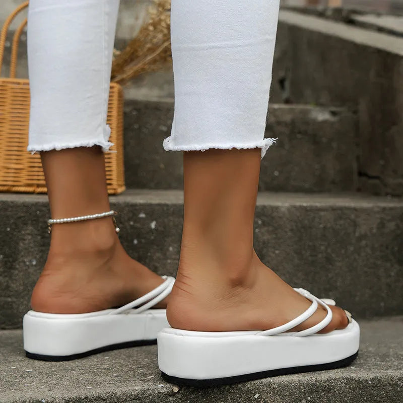 Women's white thick sole flip-flops with a herringbone rubber outsole on a sandy beach